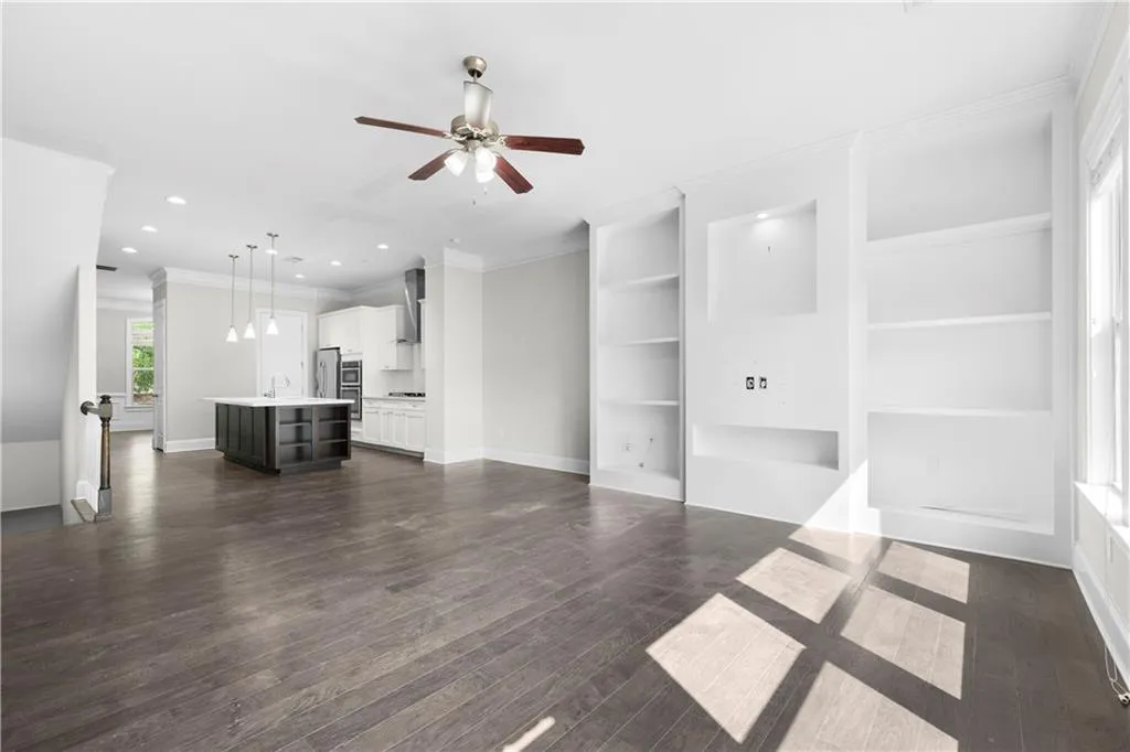 Unfurnished living room featuring built in features, ornamental molding, dark wood-style floors, a ceiling fan, and recessed lighting