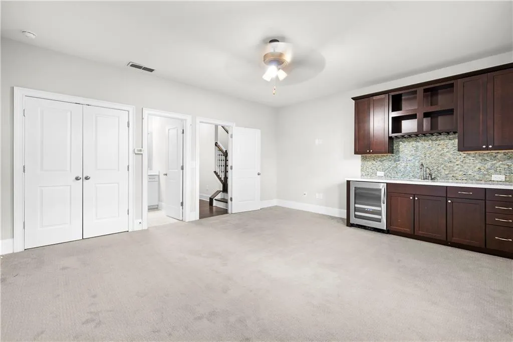 Kitchen with dark brown cabinets, beverage cooler, open shelves, and light colored carpet