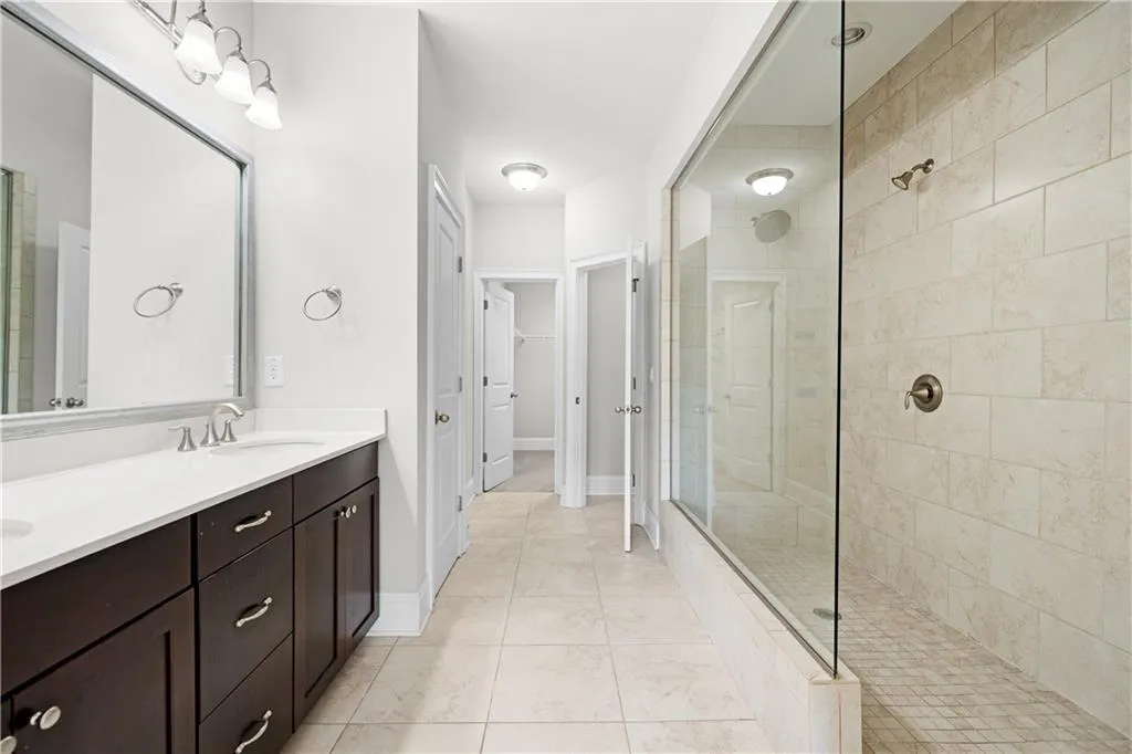 Full bath with walk in shower, double vanity, a walk in closet, and light tile patterned floors