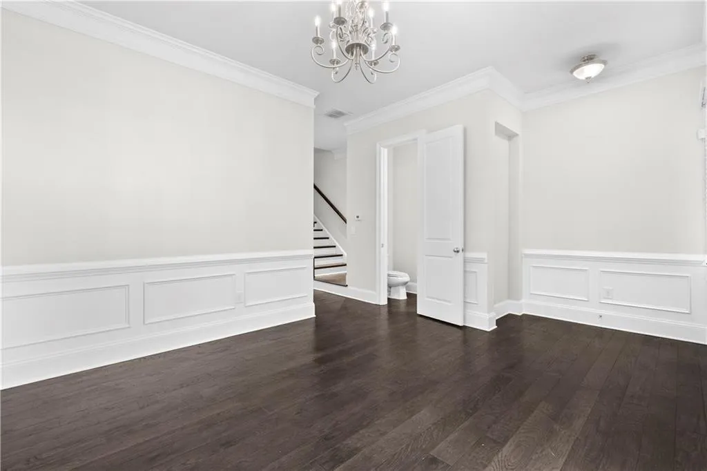 Empty room with ornamental molding, a chandelier, stairs, dark wood-type flooring, and a decorative wall