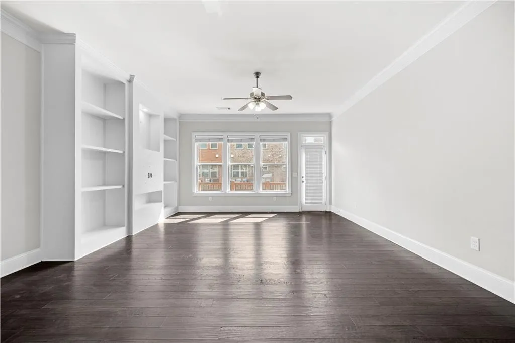 Spare room with crown molding, built in features, dark wood finished floors, and ceiling fan