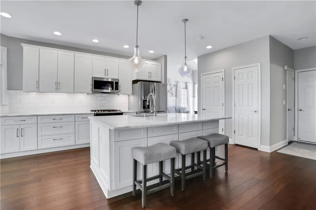 Kitchen featuring white cabinets, tasteful backsplash, decorative light fixtures, stainless steel appliances, and dark hardwood / wood-style floors Kitchen featuring white cabinets, tasteful backsplash, decorative light fixtures, stainless steel appliances, and dark hardwood / wood-style floors
