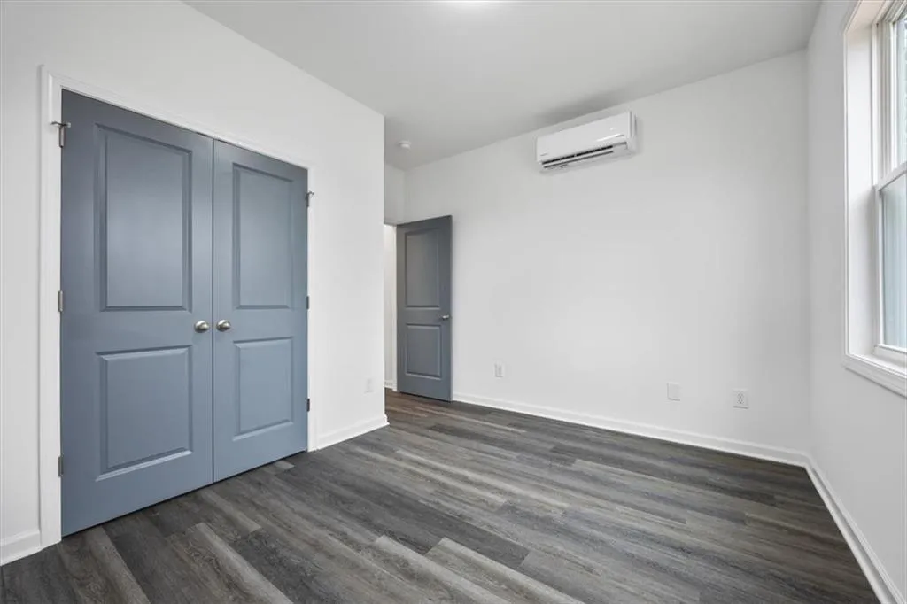 Unfurnished bedroom with a wall mounted AC, dark wood-type flooring, and a closet