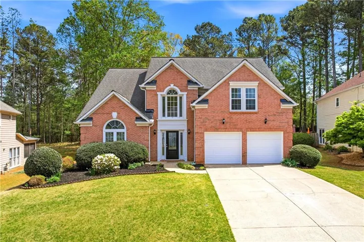 Traditional-style house featuring brick siding, driveway, a front yard, an attached garage, and roof with shingles