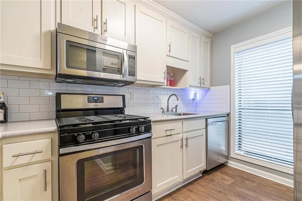 Kitchen featuring tasteful backsplash, white cabinets, stainless steel appliances, sink, and wood-type flooring