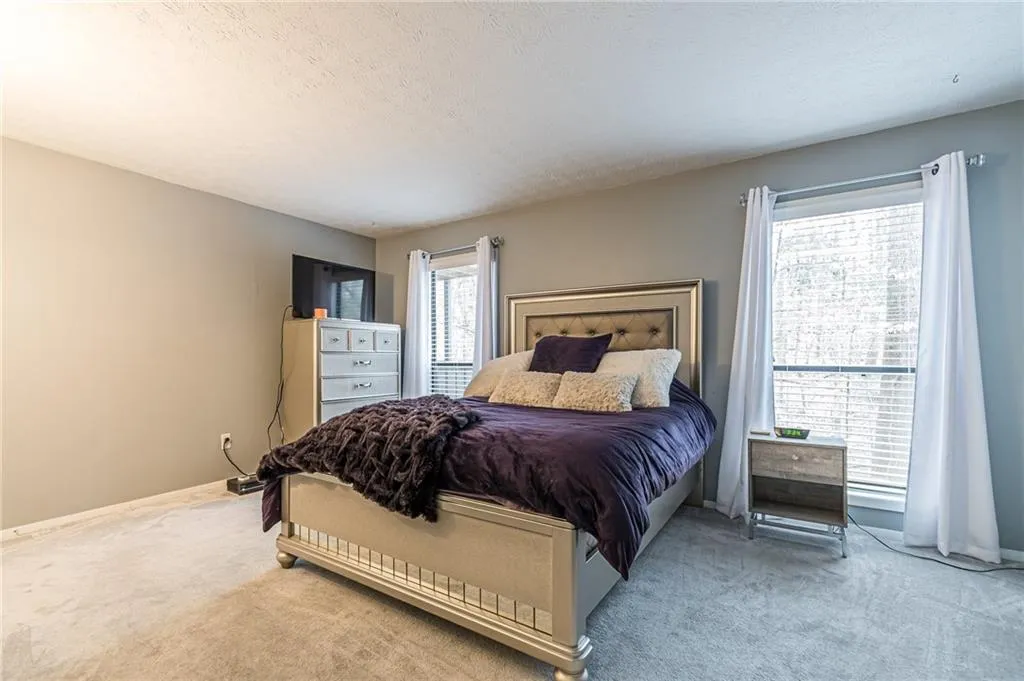 Bedroom with light colored carpet and multiple windows