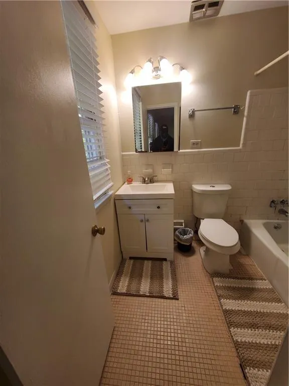 Full bath featuring light tile patterned floors, vanity, bathtub / shower combination, and tile walls