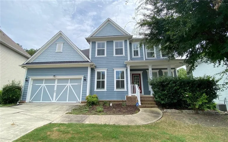 Two-story residence featuring light blue siding with white trim, a covered front porch, and a two-car garage with decorative paneling