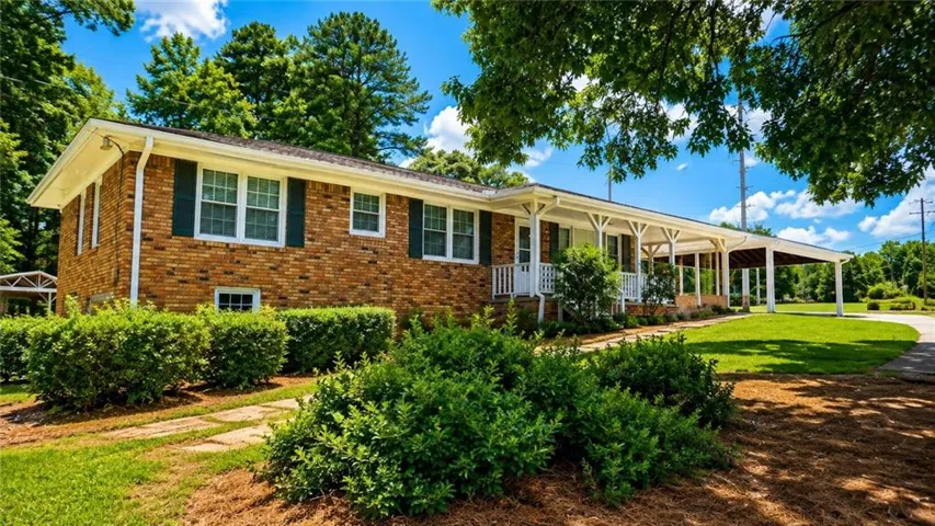 Brick exterior with dark shutters, covered front porch, carport, and manicured landscaping