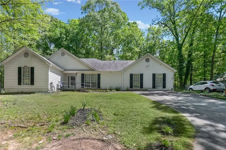 Charming ranch-style residence featuring a spacious front lawn with mature landscaping, a covered front porch with multiple entry points, composite or vinyl siding exterior, black shutters and trim detailing, and a paved driveway