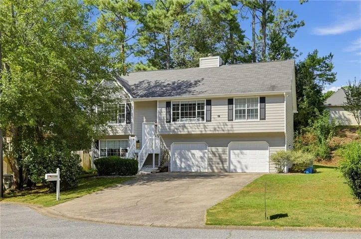 Split-level residence featuring a two-car garage, front porch with white railings, a bay window, and mature landscaping