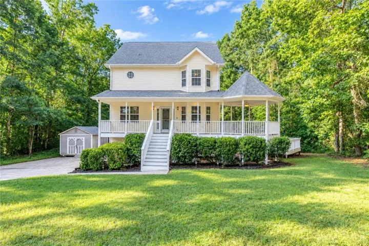 Two-story residence featuring a covered front porch, an integrated gazebo, a detached storage shed, and a driveway
