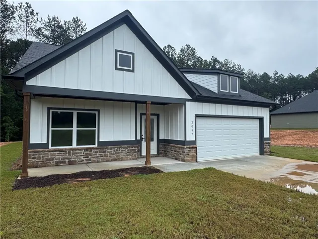 Modern farmhouse-style exterior featuring white board and batten siding, dark trim, a stone veneer foundation accent, an attached two-car garage, and a covered front entry