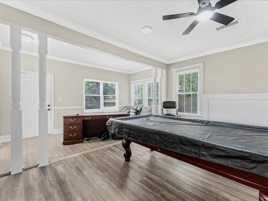 Playroom with wood finished floors, a textured ceiling, healthy amount of natural light, crown molding, and pool table