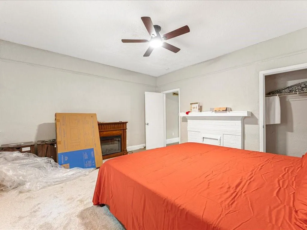 Carpeted bedroom featuring a closet, a glass covered fireplace, and a ceiling fan