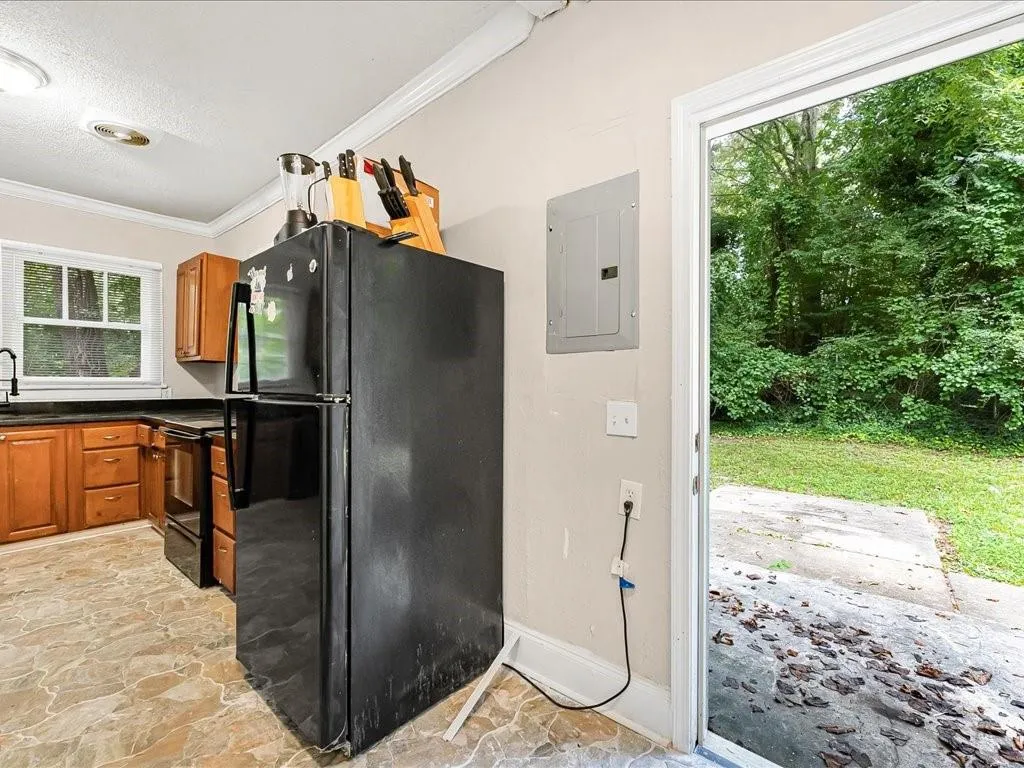 Kitchen with black appliances, light stone finish floors, ornamental molding, brown cabinets, and electric panel