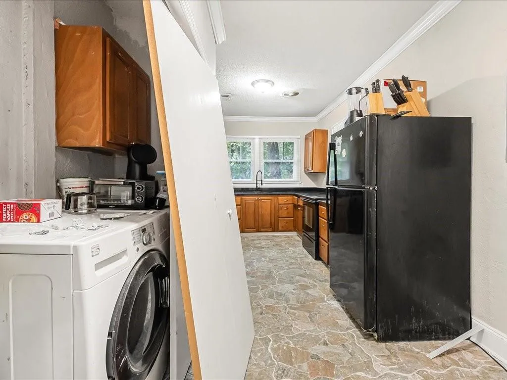 Laundry area with washer / clothes dryer, ornamental molding, light stone finish floors, and a textured ceiling