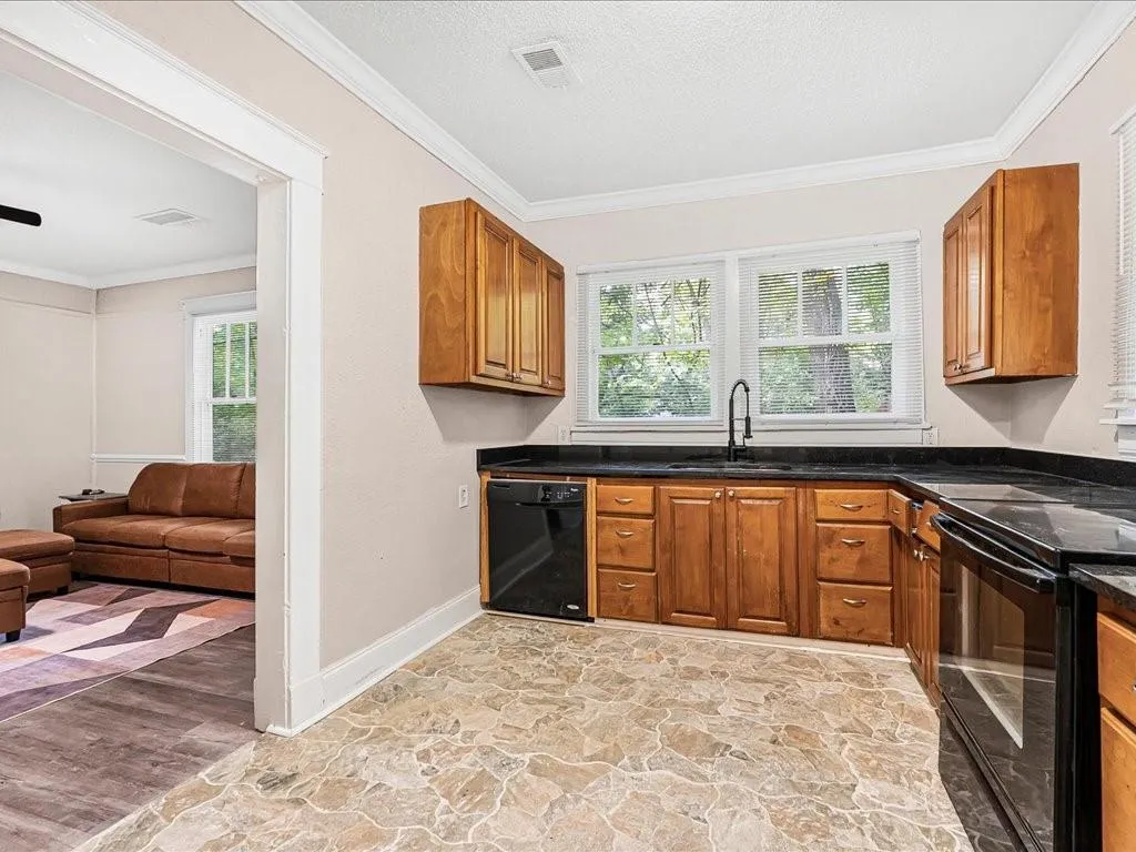 Kitchen with crown molding, brown cabinetry, plenty of natural light, black appliances, and a textured ceiling