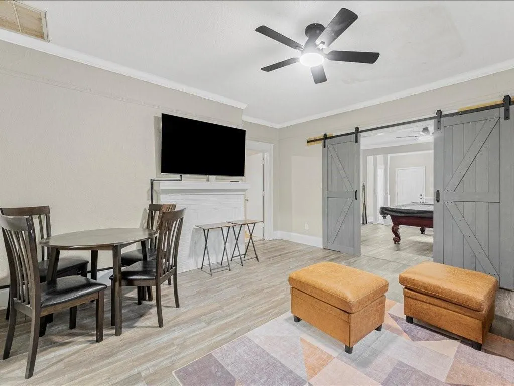 Living room featuring ceiling fan, crown molding, a barn door, and light wood-type flooring