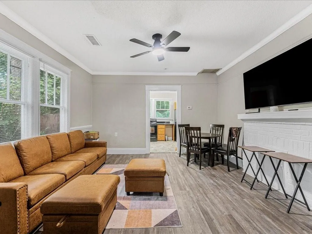 Living area featuring light wood-style flooring, ornamental molding, a textured ceiling, a ceiling fan, and a brick fireplace