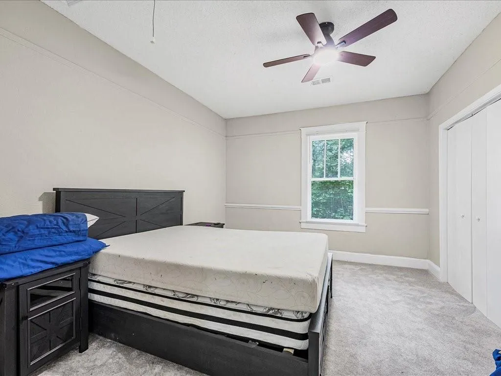 Bedroom with light colored carpet, a ceiling fan, a closet, and a textured ceiling