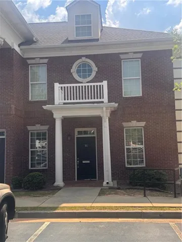 Brick exterior featuring a portico entry with round columns, a second-story balcony, a prominent dormer, and a circular window accent
