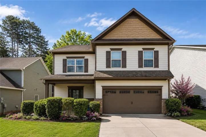 Two-story residence featuring light-colored siding with dark trim accents, a two-car garage, and a covered front porch