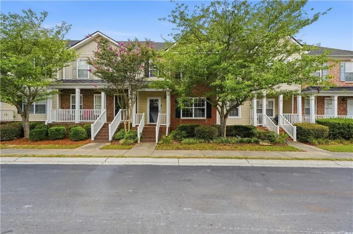 Townhome exterior featuring brick and siding accents, a covered front porch, white railings, and mature landscaping