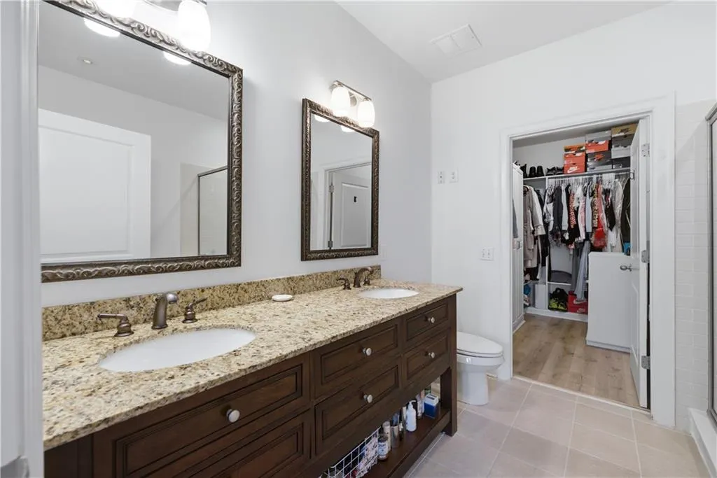 Full bathroom featuring double vanity, a stall shower, light tile patterned floors, and a walk in closet