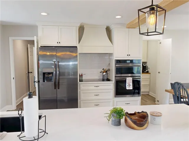 White kitchen cabinetry, stainless steel refrigerator, white subway tile backsplash, built-in double ovens, and recessed lighting