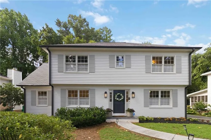 White exterior siding with light gray shutters, dark gray front door, and a paved walkway leading to the entrance