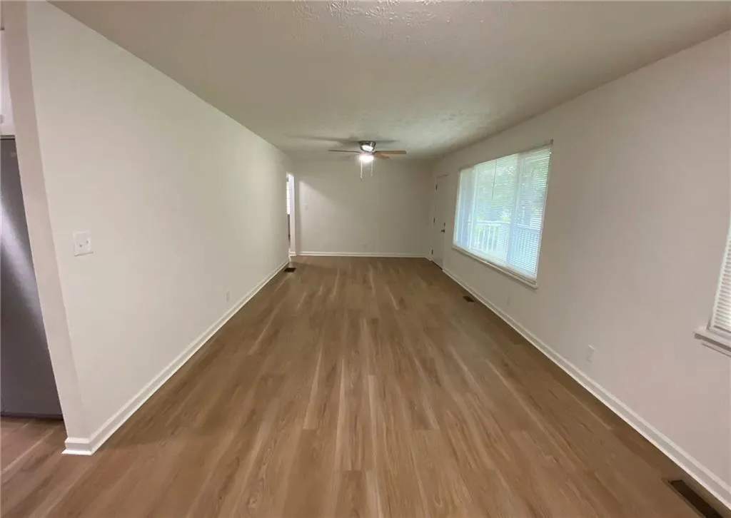 Unfurnished living room with wood finished floors, a textured ceiling, and a ceiling fan