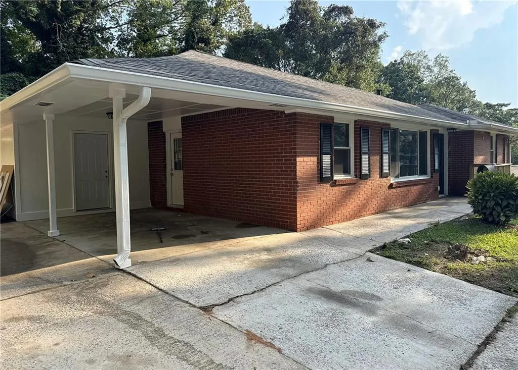 View of side of property featuring brick siding, driveway, roof with shingles, and an attached carport