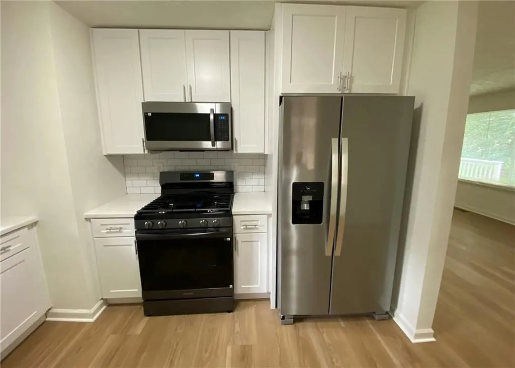 Kitchen featuring stainless steel appliances, white cabinetry, light wood-style floors, and decorative backsplash