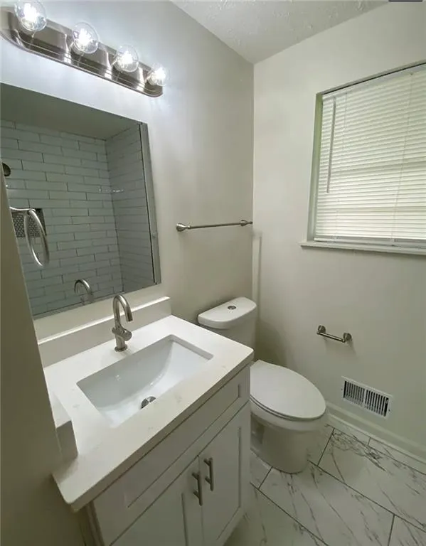 Full bathroom featuring vanity, a textured ceiling, a tile shower, and light marble finish flooring