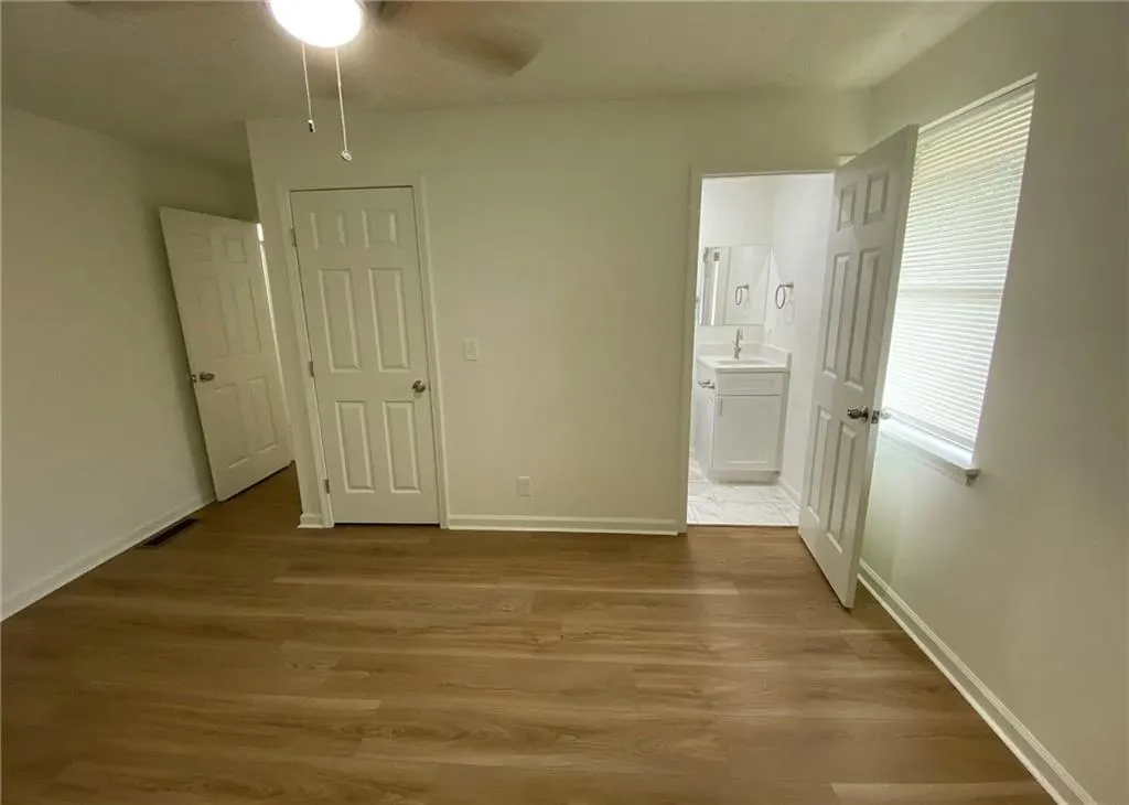 Unfurnished bedroom with dark wood-type flooring, connected bathroom, and a ceiling fan