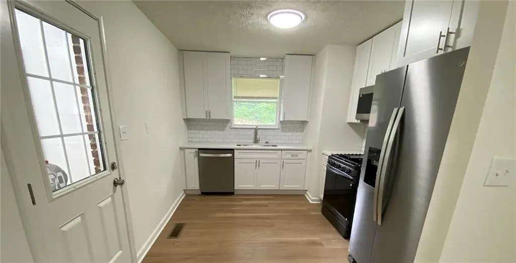Kitchen featuring stainless steel appliances, decorative backsplash, white cabinets, light wood-style floors, and a textured ceiling