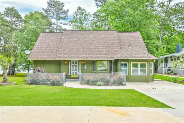 Green-sided residence featuring a brown shingle roof and a concrete driveway