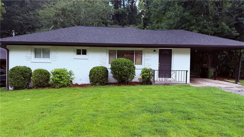 White brick exterior with a dark asphalt shingle roof, front entry with a black security door, and an attached carport
