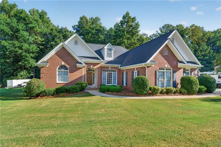 Brick exterior with white gables, dark shingle roof, arched transom window, and mature landscaping