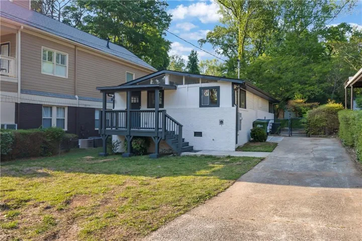Rear exterior featuring a covered porch with dark gray railings and stairs, a white brick facade, dark trim, and a concrete driveway