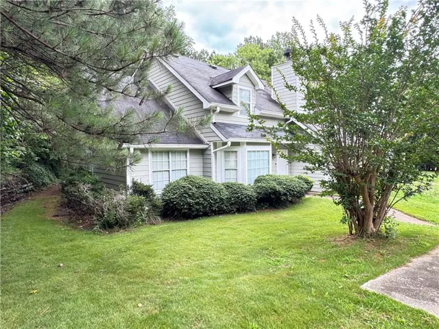 View of side of property featuring a shingled roof, a chimney, and a yard
