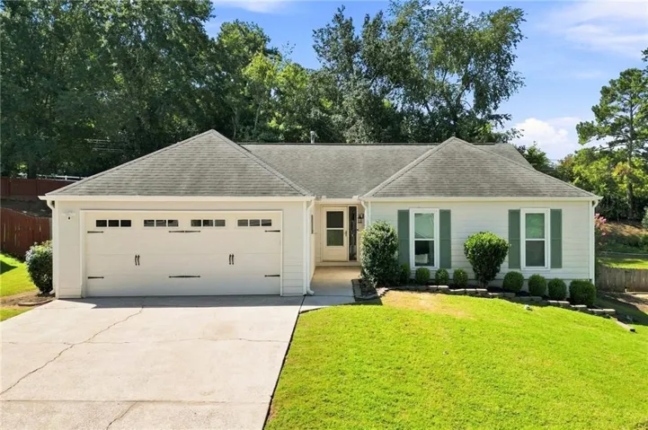 White exterior siding with green window shutters, attached two-car garage, concrete driveway, and front yard landscaping