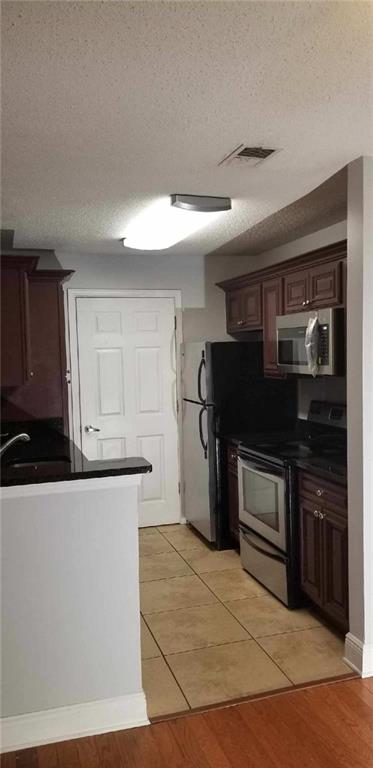 Kitchen with dark brown cabinetry, a textured ceiling, light hardwood / wood-style floors, and appliances with stainless steel finishes