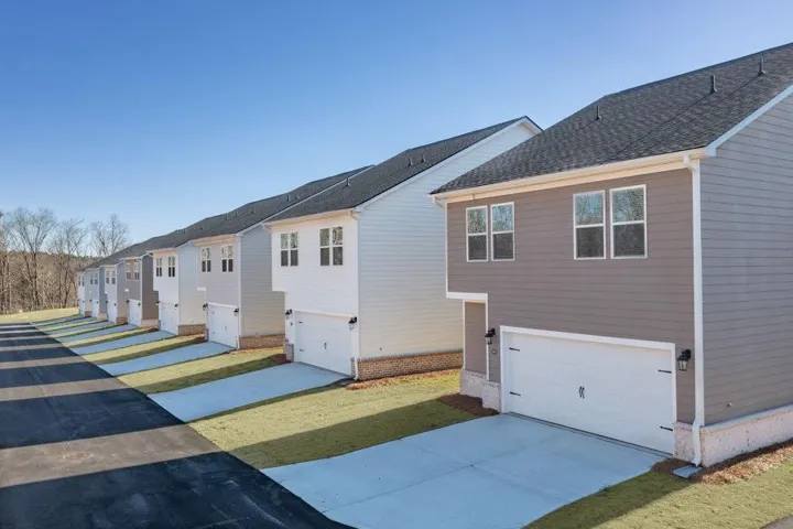 Newly constructed townhomes featuring durable siding, asphalt shingle roofing, and attached garages with concrete driveways