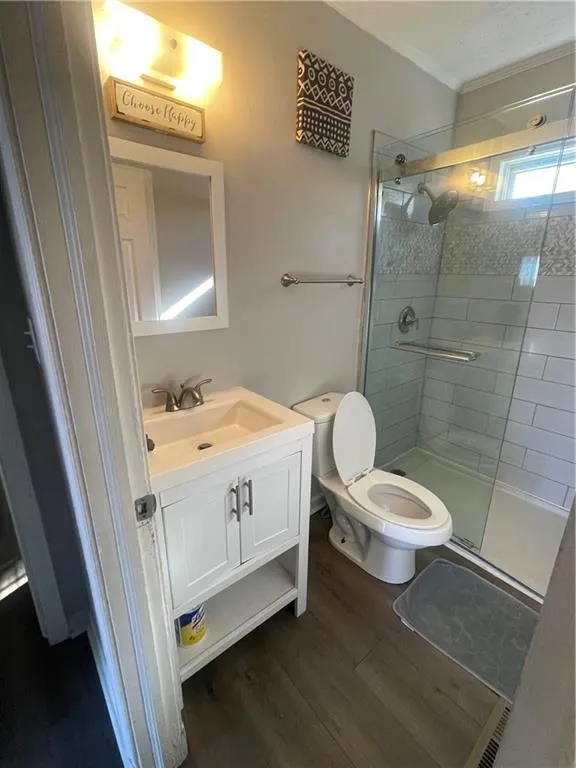 Bathroom with hardwood / wood-style floors, vanity, toilet, and a shower with shower door