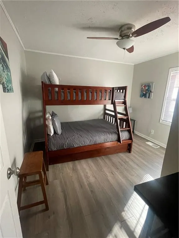 Bedroom with a textured ceiling, ceiling fan, wood-type flooring, and ornamental molding