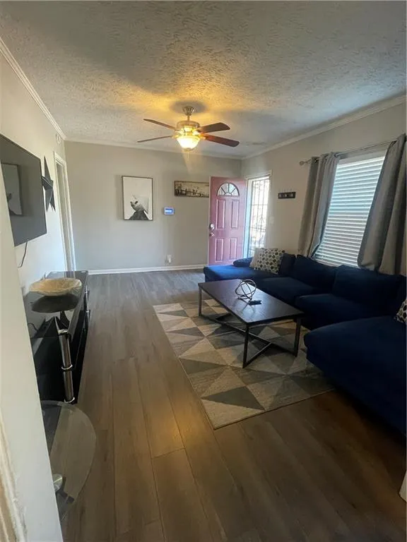 Living room featuring ceiling fan, dark hardwood / wood-style flooring, a textured ceiling, and ornamental molding