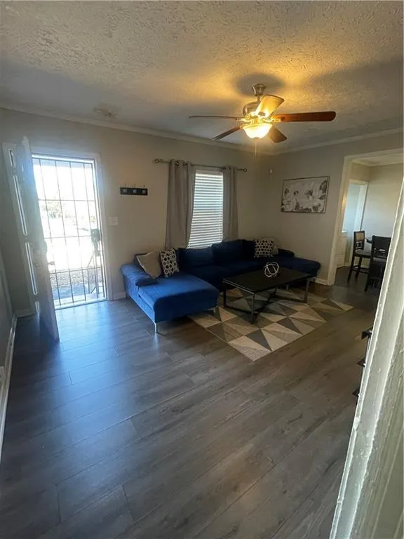 Living room featuring a textured ceiling, dark hardwood / wood-style floors, ceiling fan, and crown molding