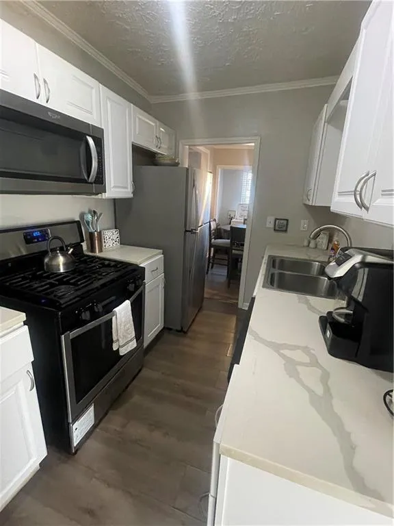 Kitchen with stove, sink, crown molding, a textured ceiling, and white cabinetry